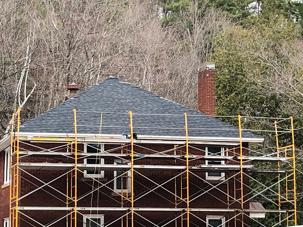 Large red home in a wooded area with the whole side pictured having construction rafting around it ready for work.